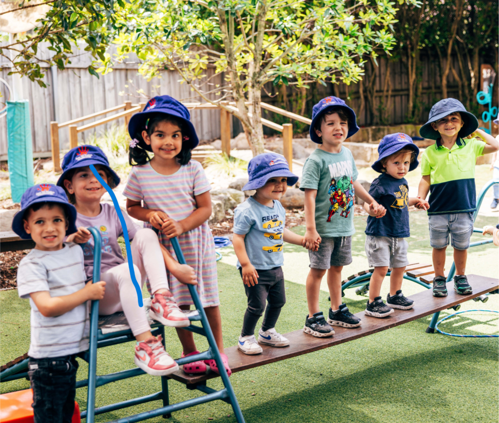 A group of children standing, holding hands on a piece of apparatus in the Care for Kindies garden.